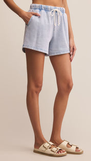 Light blue denim-look shorts with a white drawstring waist and two front pockets, paired with cream double-buckle sandals.