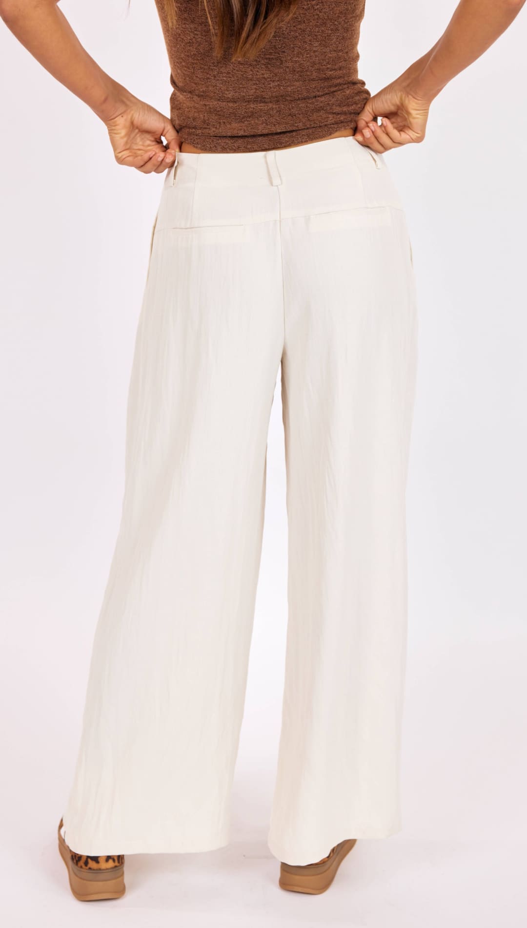 Cream-colored wide-leg trousers with a smooth, flowing fabric and two back pockets.