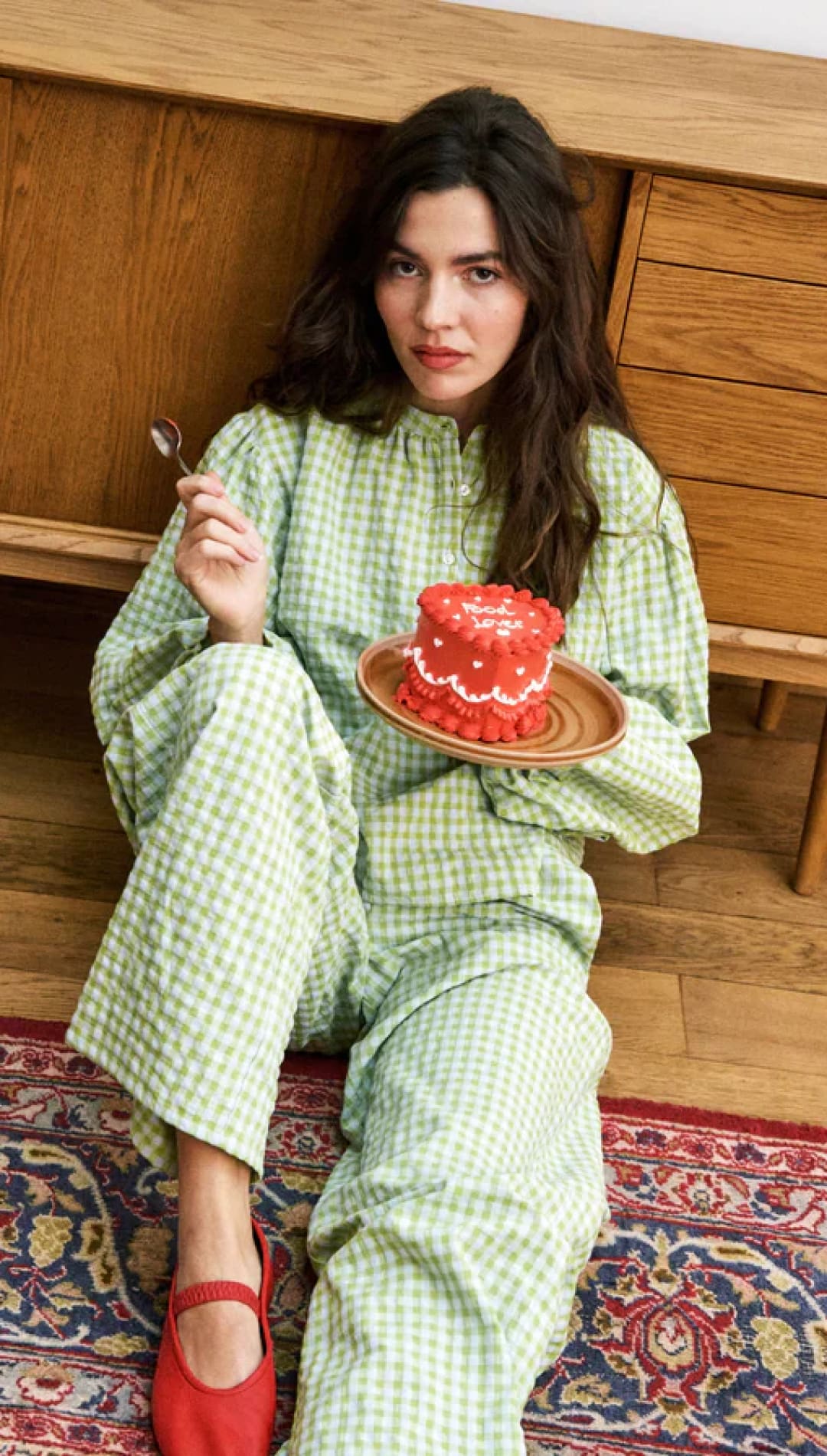 Woman in green gingham pajamas holding a red cake.