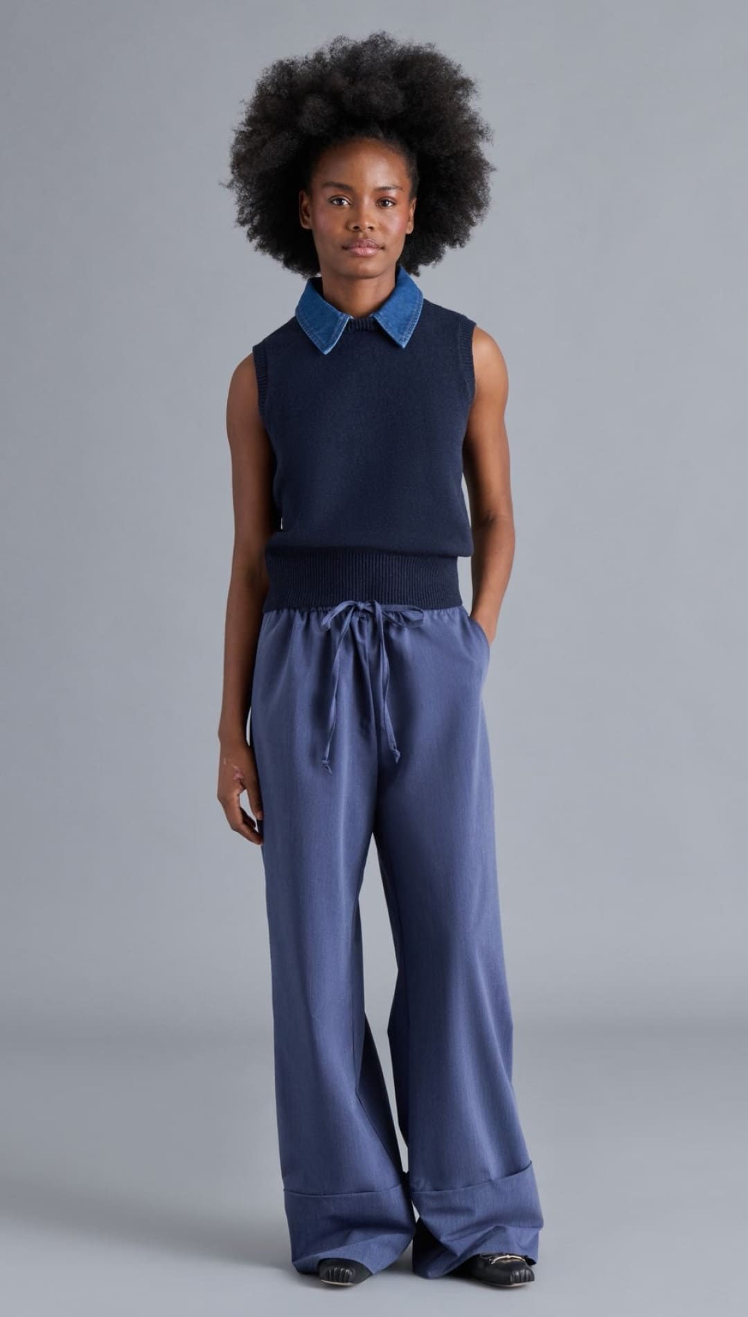 A woman’s navy blue sleeveless sweater with a denim collar and wide-leg blue trousers.