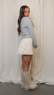 Woman in a light blue sweater, floral skirt, and knee-high boots.