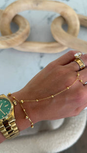Gold-tone wristwatch with a vibrant green dial and diamond hour markers, paired with matching gold-toned chain bracelet featuring spherical beads.