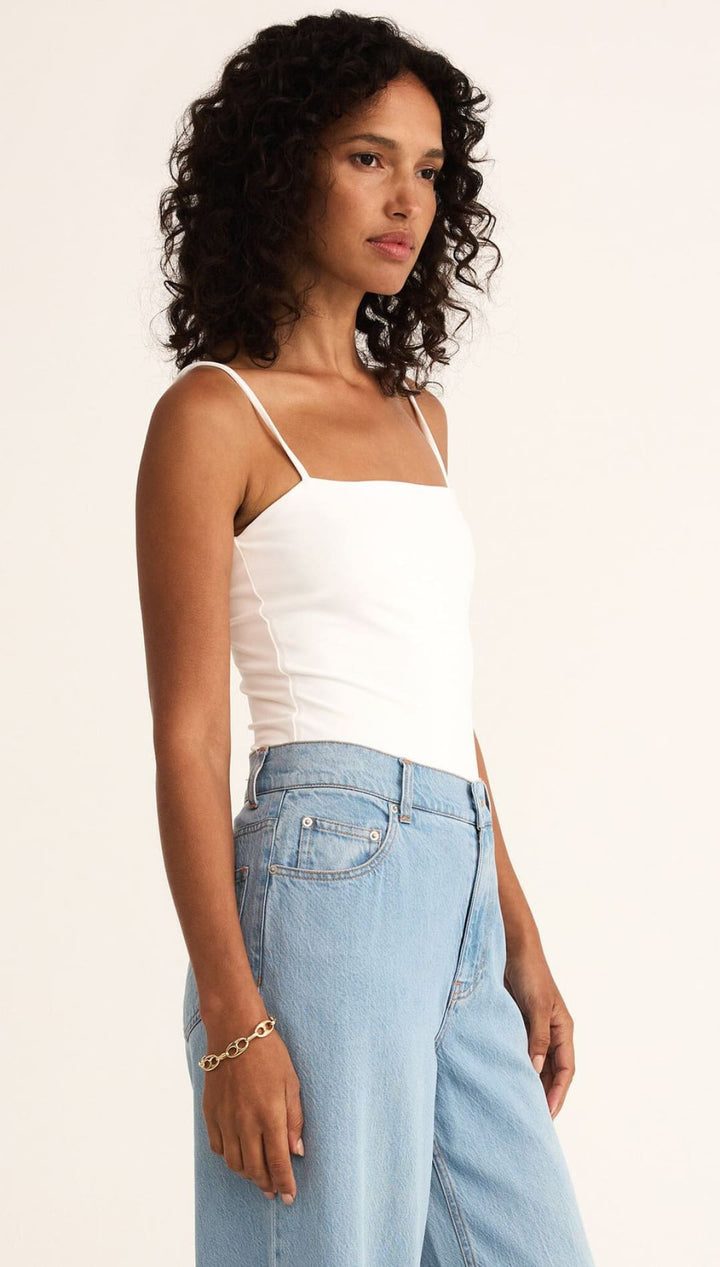 Woman wearing a white tank top and light blue jeans.