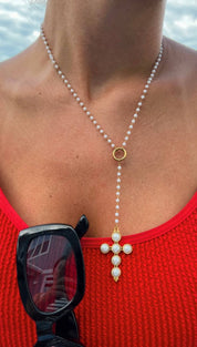A delicate pearl and gold cross necklace with a y-shaped chain design.