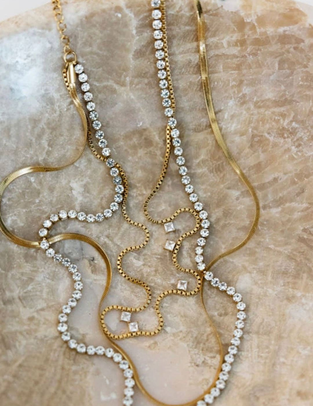 A set of three gold-toned necklaces, each adorned with clear rhinestones in varying arrangements and styles.