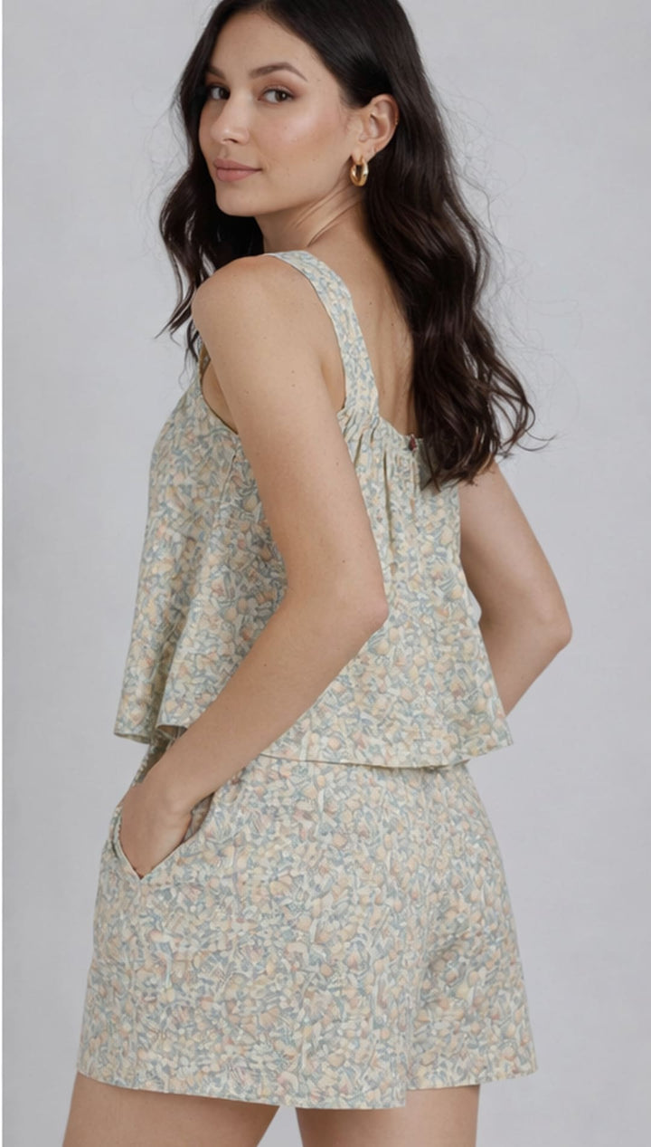 A soft, light green and white floral print sleeveless top with a ruffled hemline.