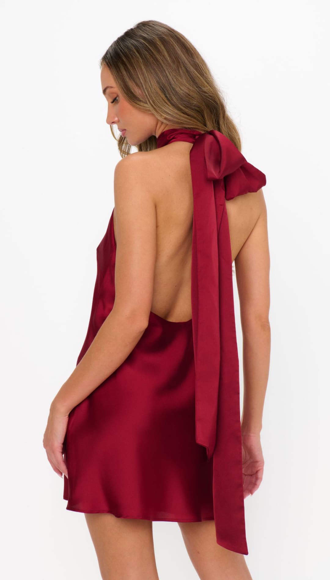 A backless, halter-neck mini dress in deep red satin with a large bow detail at the back of the neck.