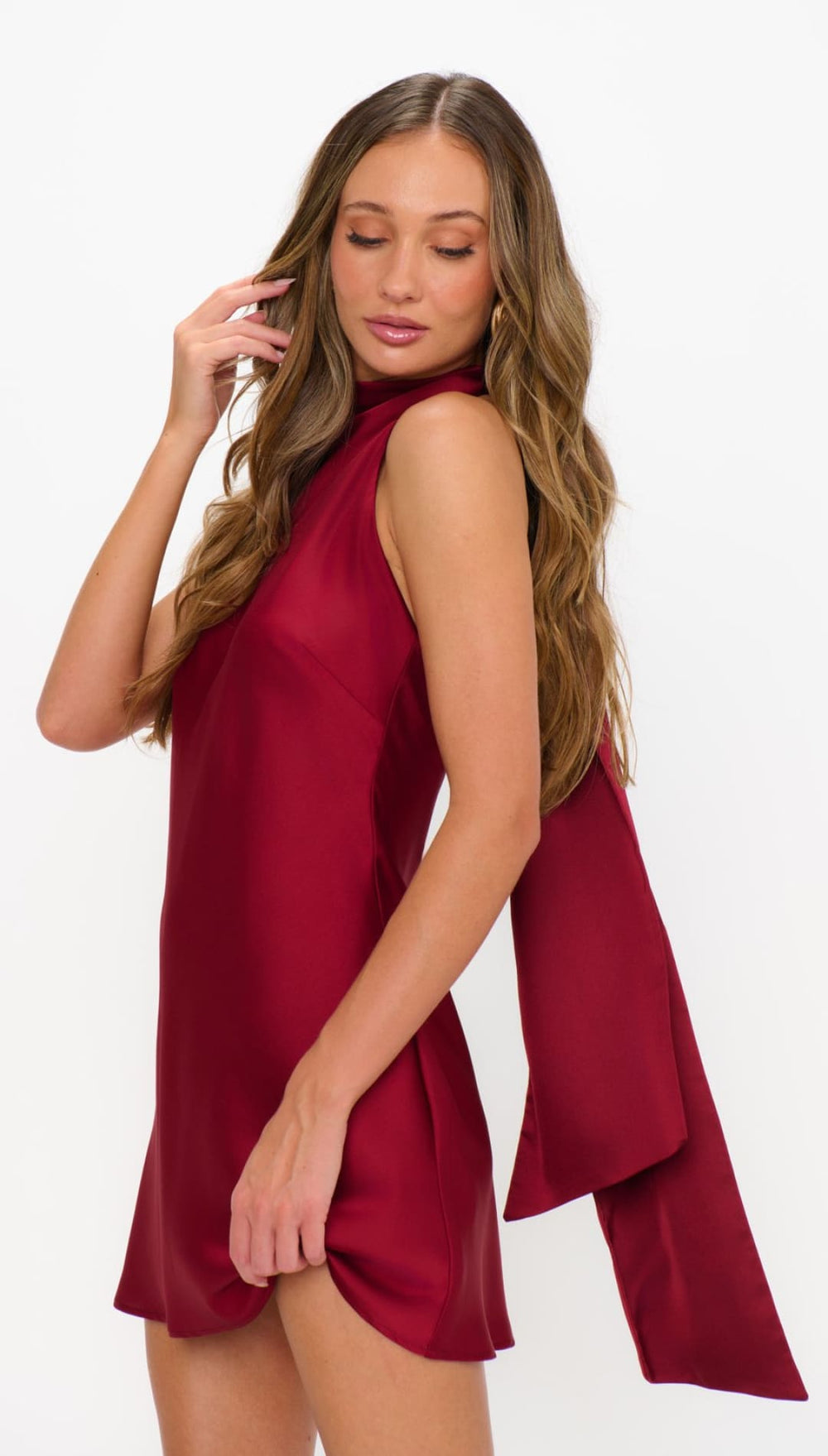 A sleeveless, high-neck mini dress in a rich burgundy color, featuring a long, flowing sash detail from the back.