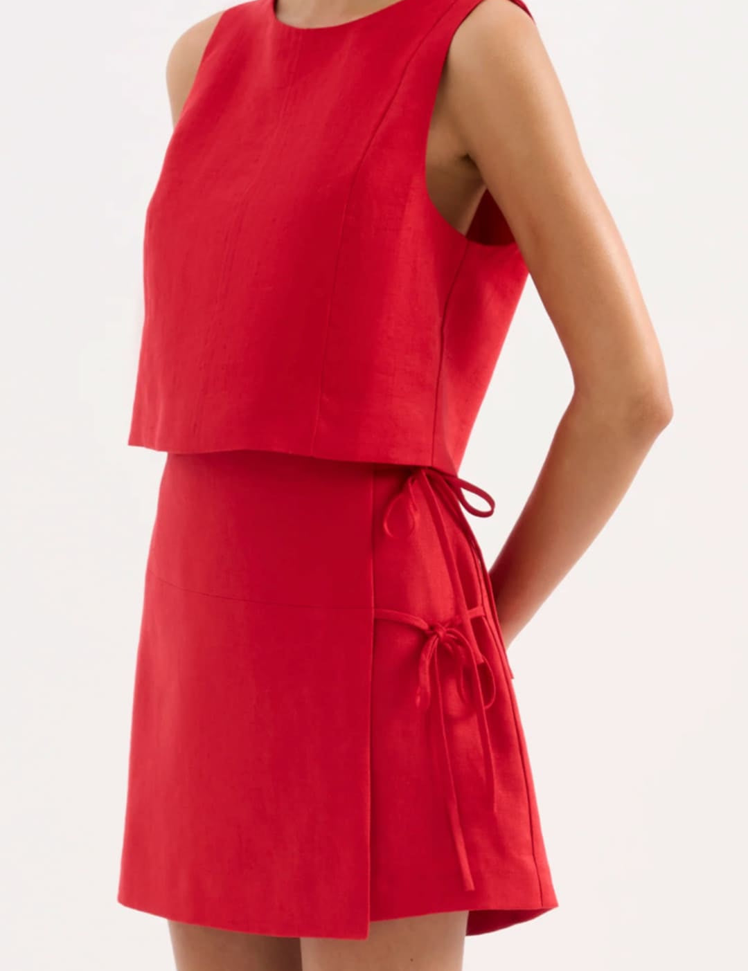 A vibrant red sleeveless two-piece outfit featuring a cropped top and flared skirt with matching fabric ties at the waist.