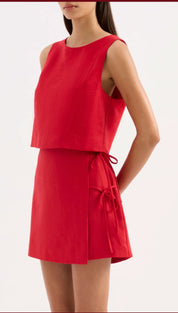 A vibrant red sleeveless two-piece outfit featuring a cropped top and flared skirt with matching fabric ties at the waist.