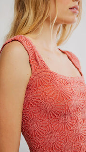 A coral-colored, textured knit top with a square neckline and wide shoulder straps.
