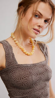 A woman wears a textured, dark gray sleeveless top with an intricate sunburst pattern.