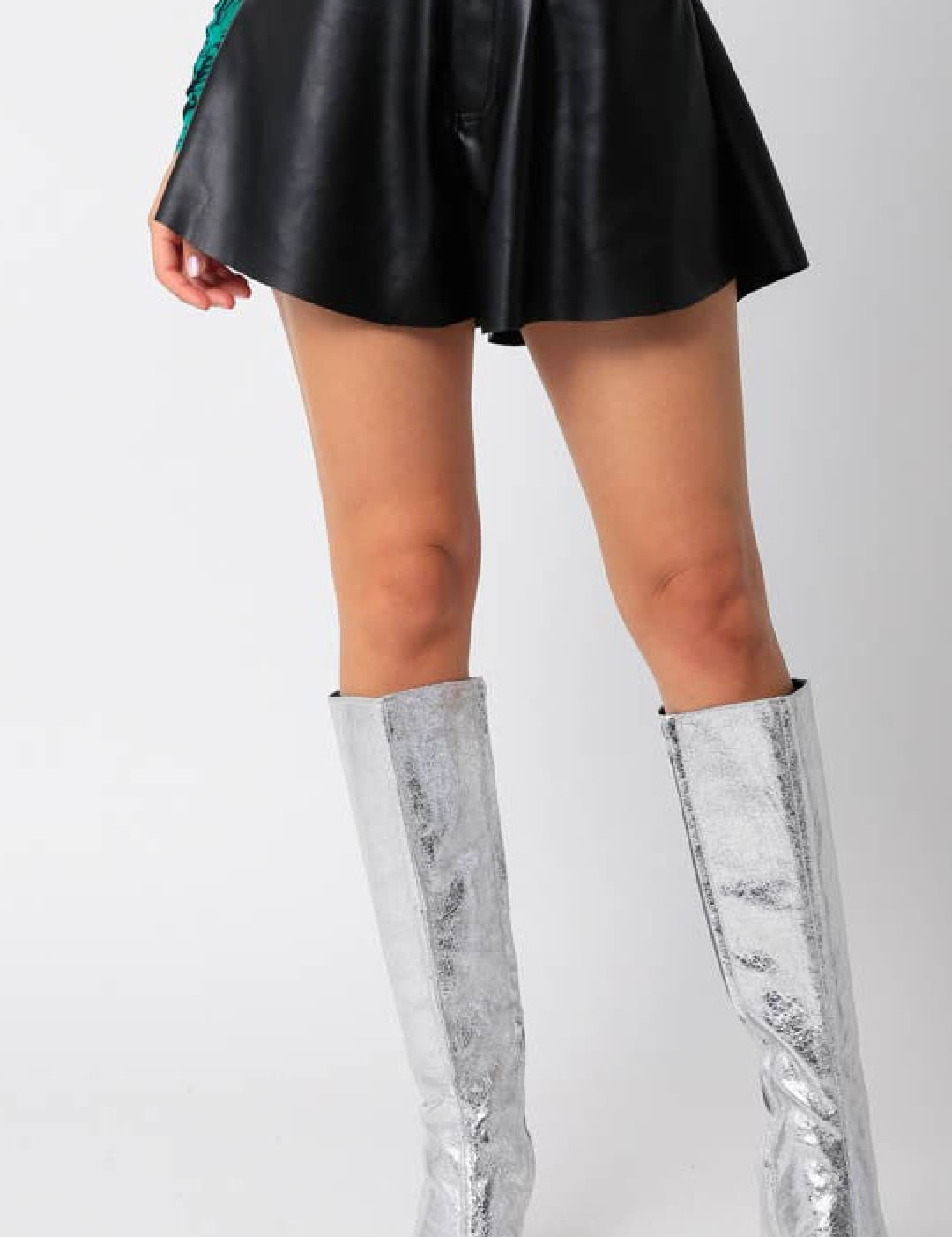 Women’s black faux leather flared shorts with silver knee-high boots.