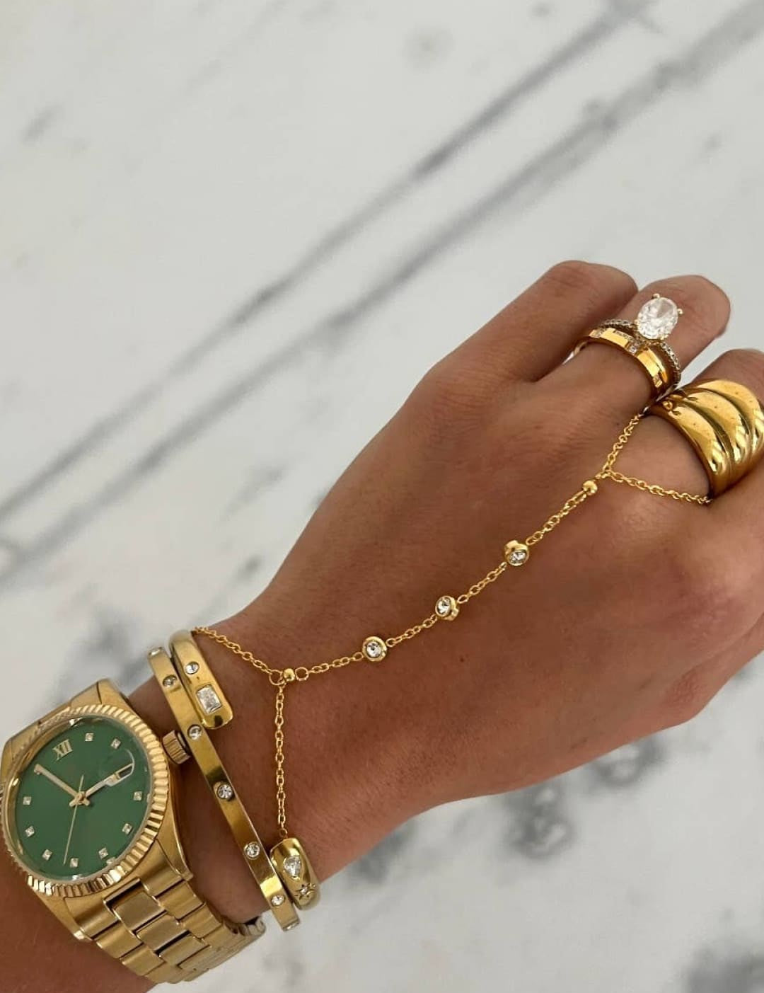 Gold-toned wristwatch with a green dial and diamond accents on the bezel, paired with matching gold bracelets and finger chains.