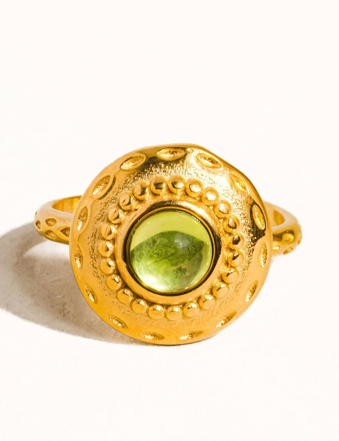 Gold-toned ring with a round, textured bezel setting a vibrant green peridot stone.