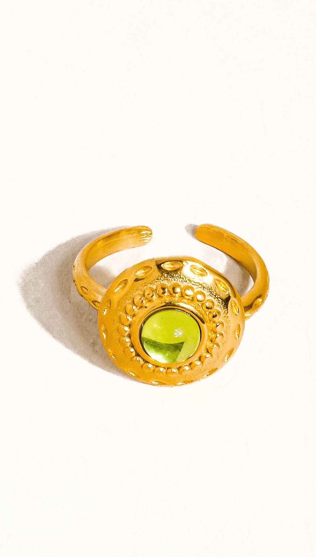Gold-toned adjustable ring featuring a round, faceted green gemstone set in an ornate, textured bezel.
