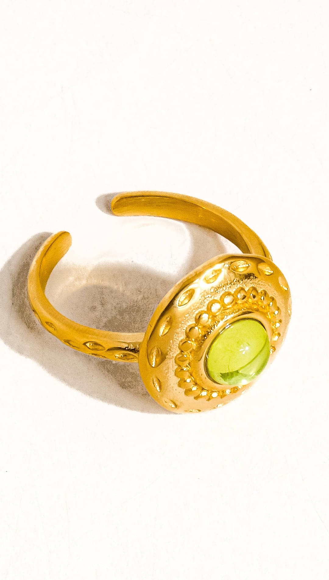 Gold-toned adjustable ring featuring a round, faceted green peridot stone set in an ornate bezel with intricate beaded detailing.