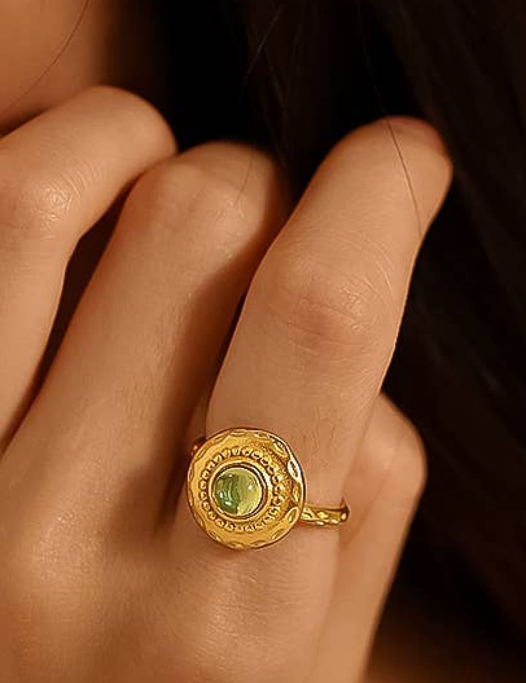 A gold-toned ring with an ornate, circular design featuring a central green gemstone.