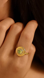 A gold-toned ring with an ornate, circular design featuring a central green gemstone.