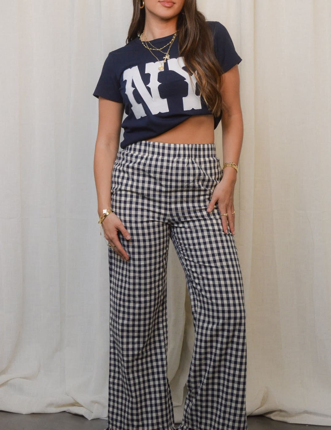 A woman in a navy ’NY’ crop top and black and white gingham wide-leg pants with ruffled hems.