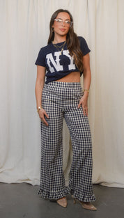 A woman in a navy ’NY’ crop top and black and white gingham wide-leg pants with ruffled hems.