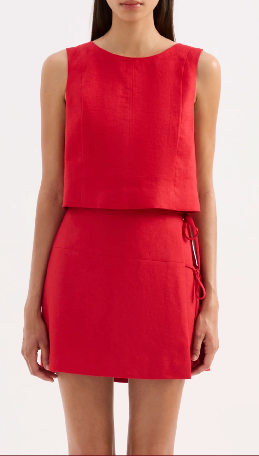 A vibrant red sleeveless two-piece outfit featuring a structured top and a flared skirt with side ties.