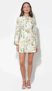 A woman wears a cream-colored floral mini dress with long sleeves and delicate lace detailing.
