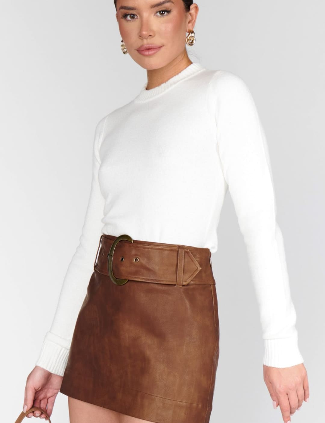 A woman wearing a white long-sleeve top and a brown mini skirt with a matching belt.