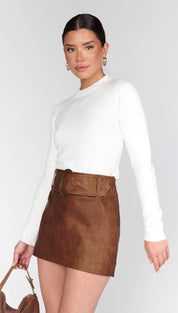 A woman wearing a white long-sleeve top and a brown mini skirt with a matching belt.