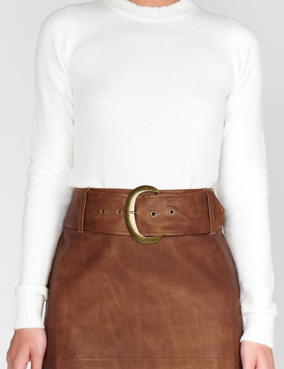 A woman wearing a white long-sleeve top and a brown leather mini-skirt with a wide belt.
