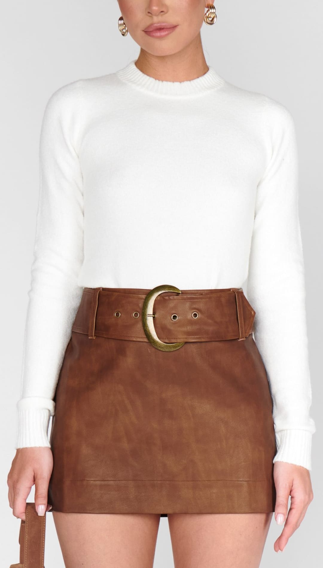 A woman wearing a white long-sleeve top and a brown leather mini-skirt with a wide belt.