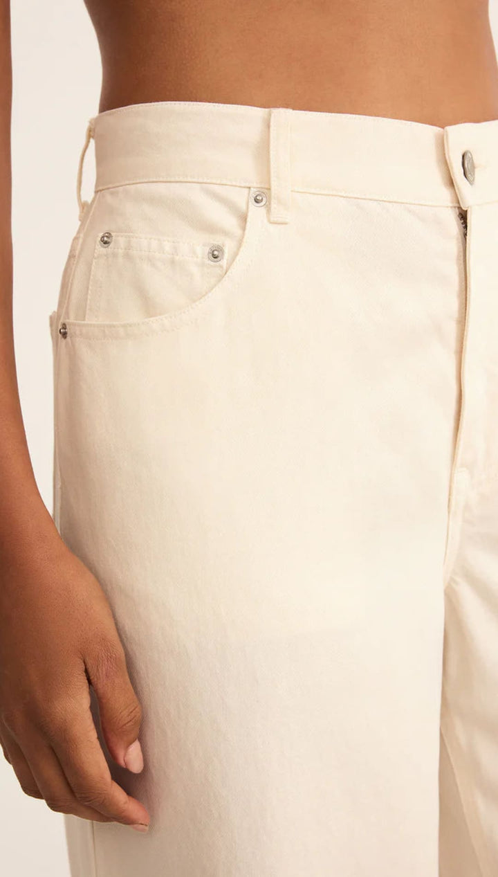 Cream-colored high-waisted pants with button details and pockets.