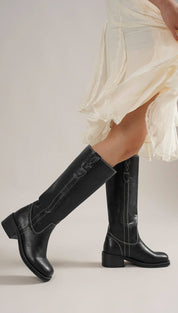 Black leather knee-high boots with white stitching and low block heels.