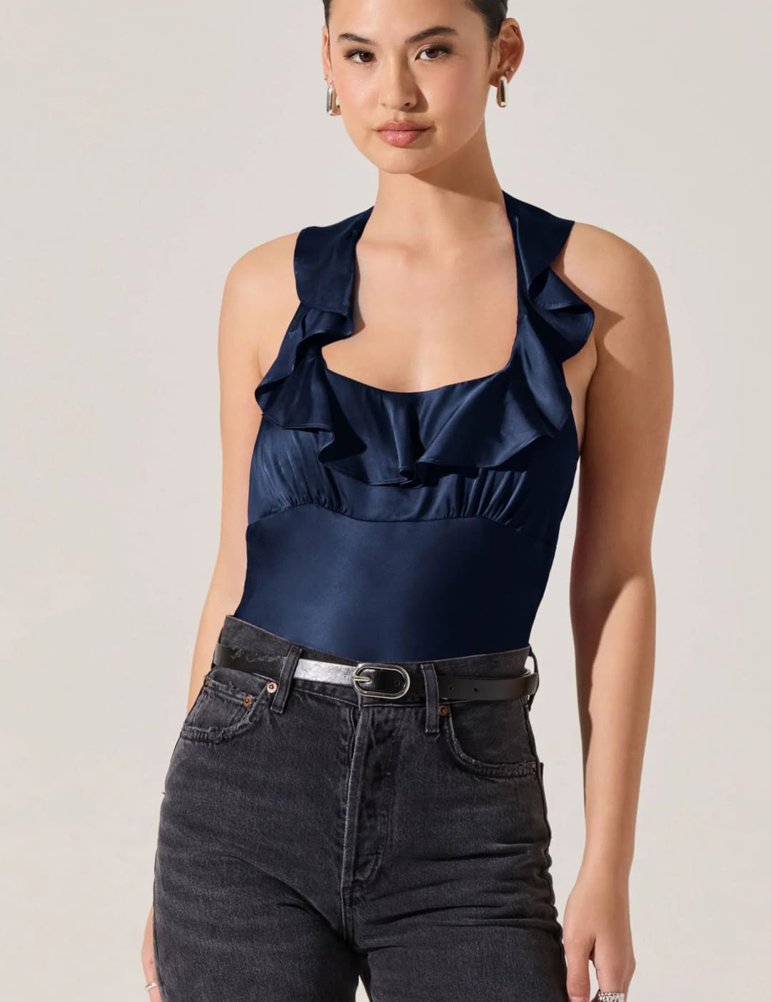 Women’s navy blue satin ruffled halter top with dark wash jeans and a silver belt.