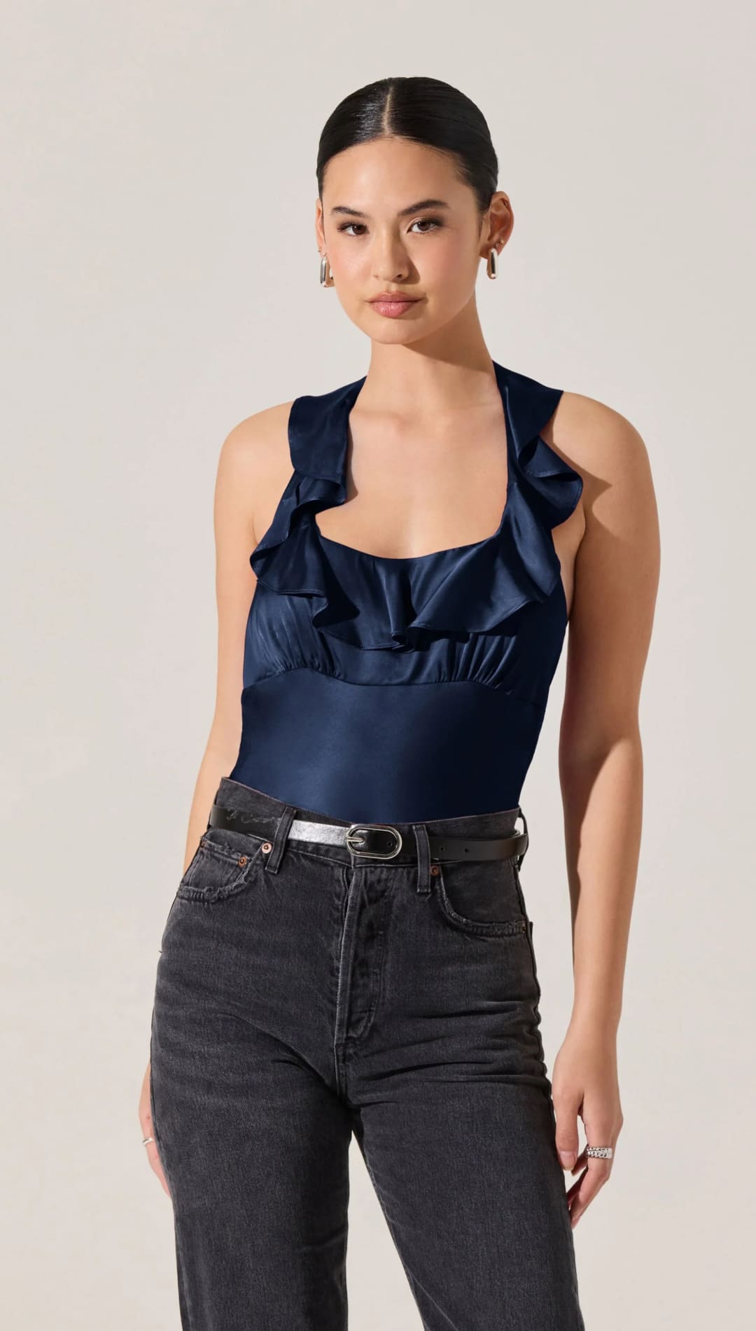 Women’s navy blue satin ruffled halter top with dark wash jeans and a silver belt.