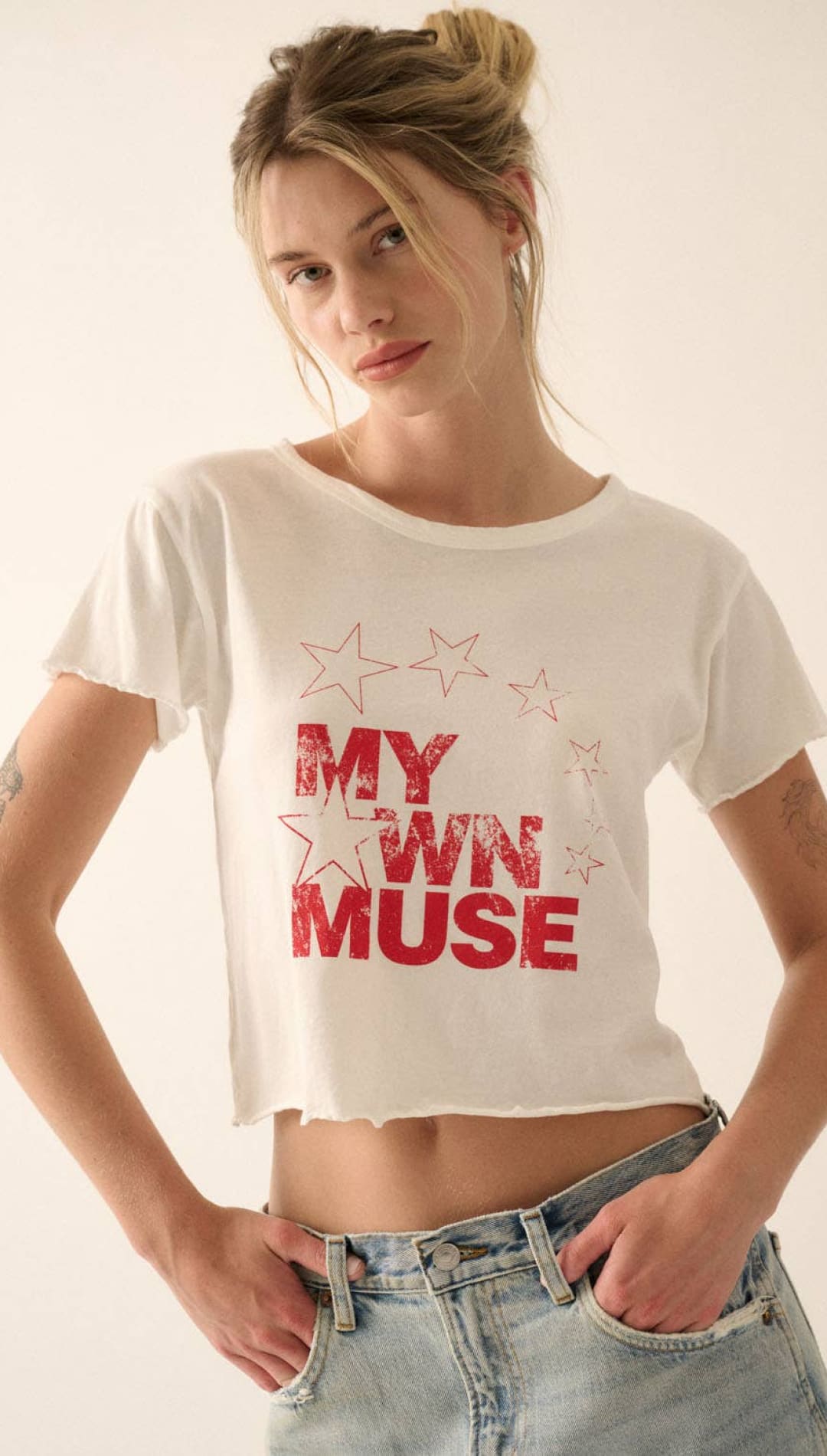 White cropped t-shirt with ’my own muse’ printed in red, surrounded by star graphics.