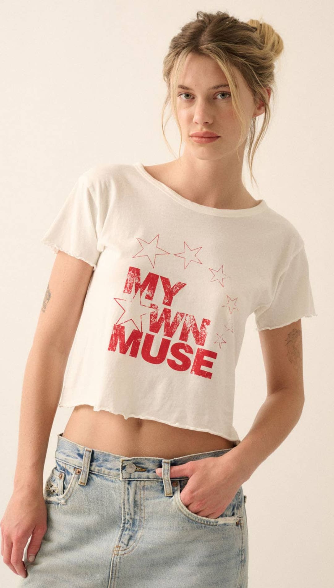White cropped t-shirt with red ’my own muse’ text and star graphics.