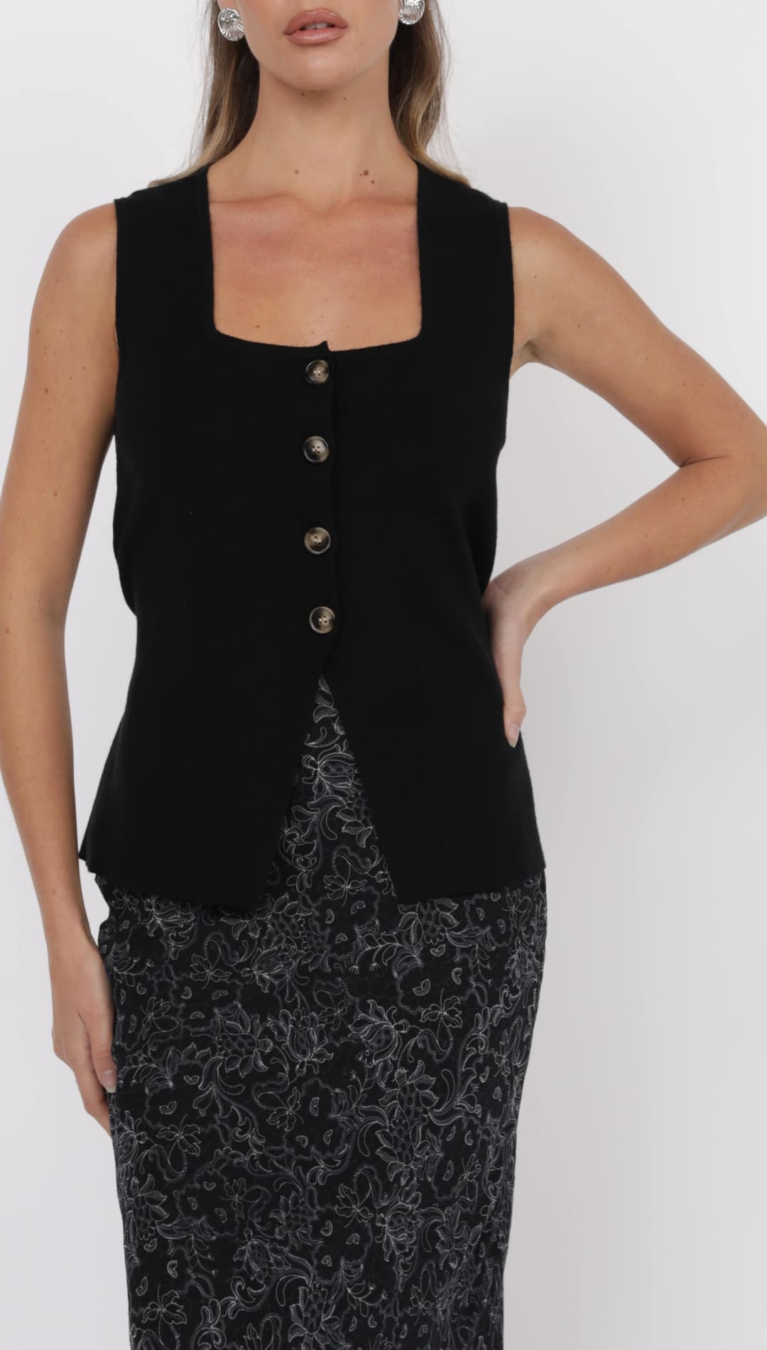 Black sleeveless top with a square neckline and a front button placket worn over a dark floral print midi skirt.
