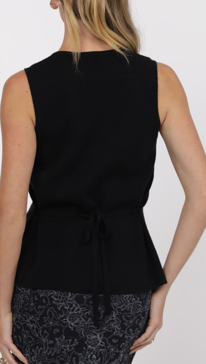 Women’s black sleeveless top with a tie-waist over a patterned skirt.