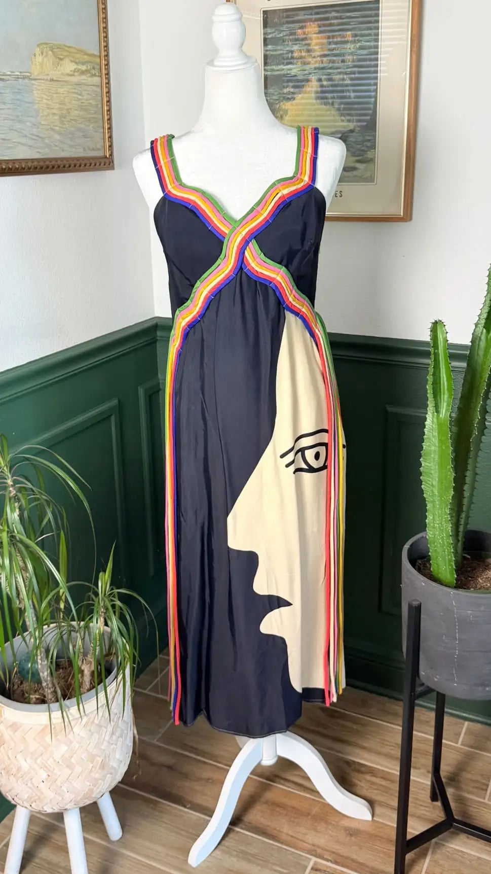 A navy blue sleeveless dress with a bold, stylized face design in cream and vibrant rainbow trim along the straps and hem.