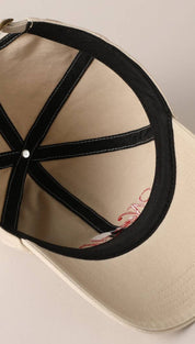 Beige baseball cap with black brim and interior straps, featuring a small red embroidered logo on the side.