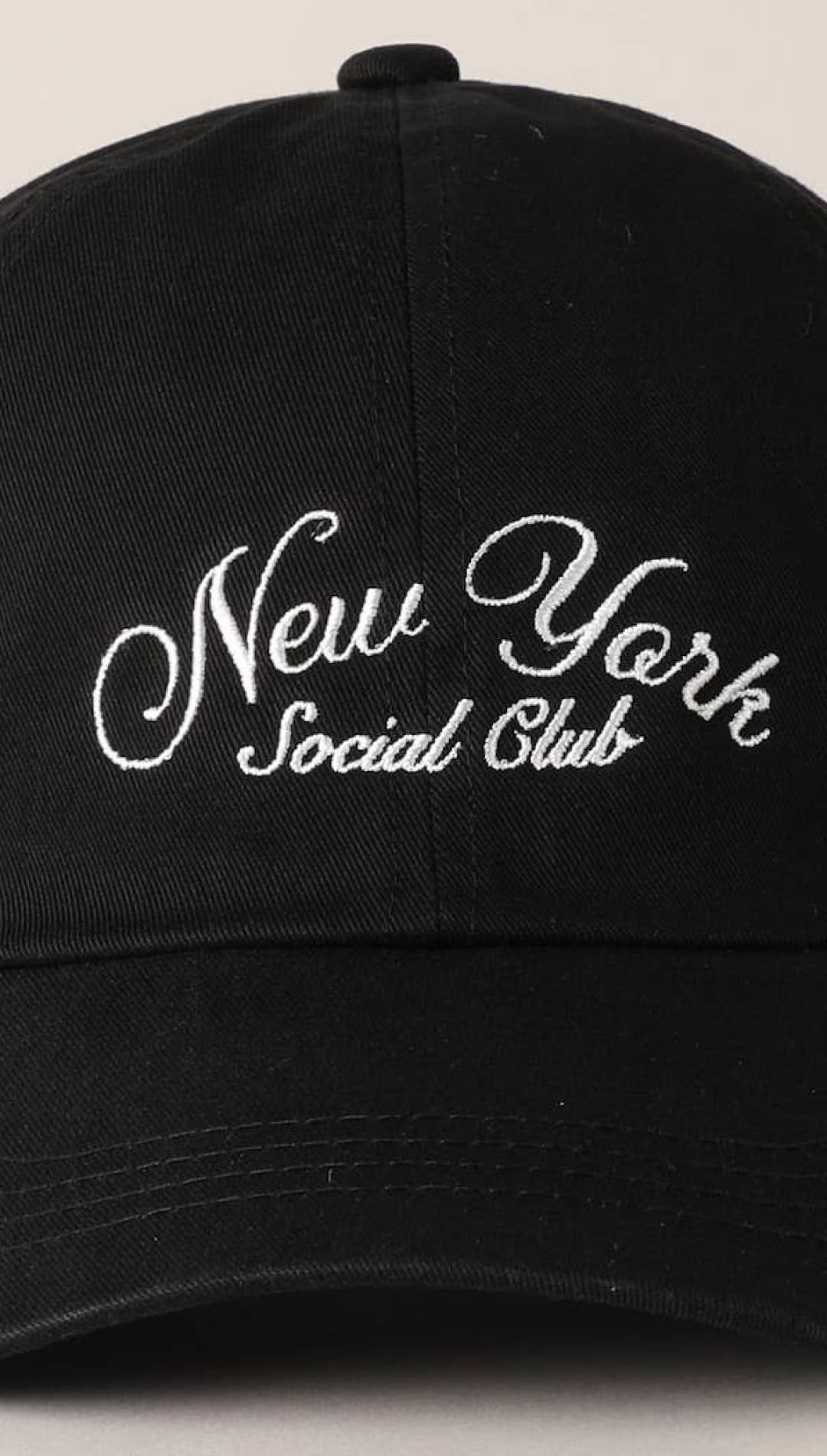 Black baseball cap with white embroidered ’new york social club’ text in a cursive script.