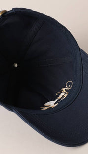 Navy blue baseball cap with gold and white embroidered design on the brim