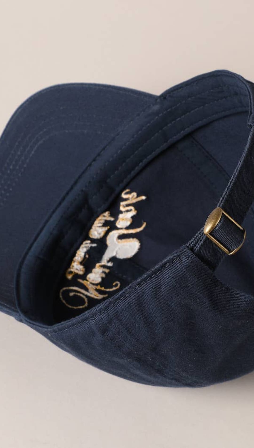 Navy blue baseball cap with gold embroidered logo and adjustable strap
