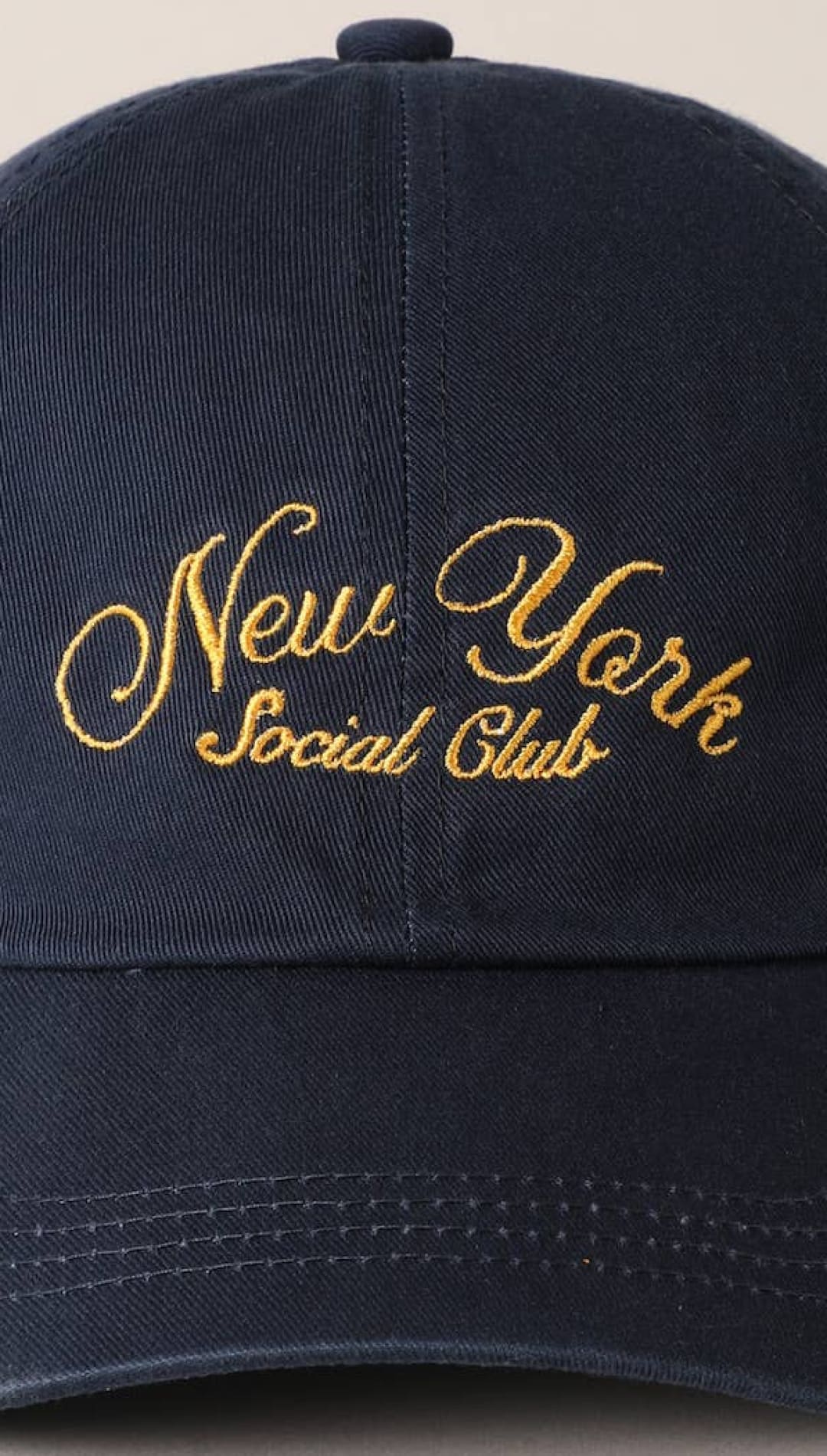 Navy blue cotton baseball cap with gold embroidered ’new york social club’ script across the front