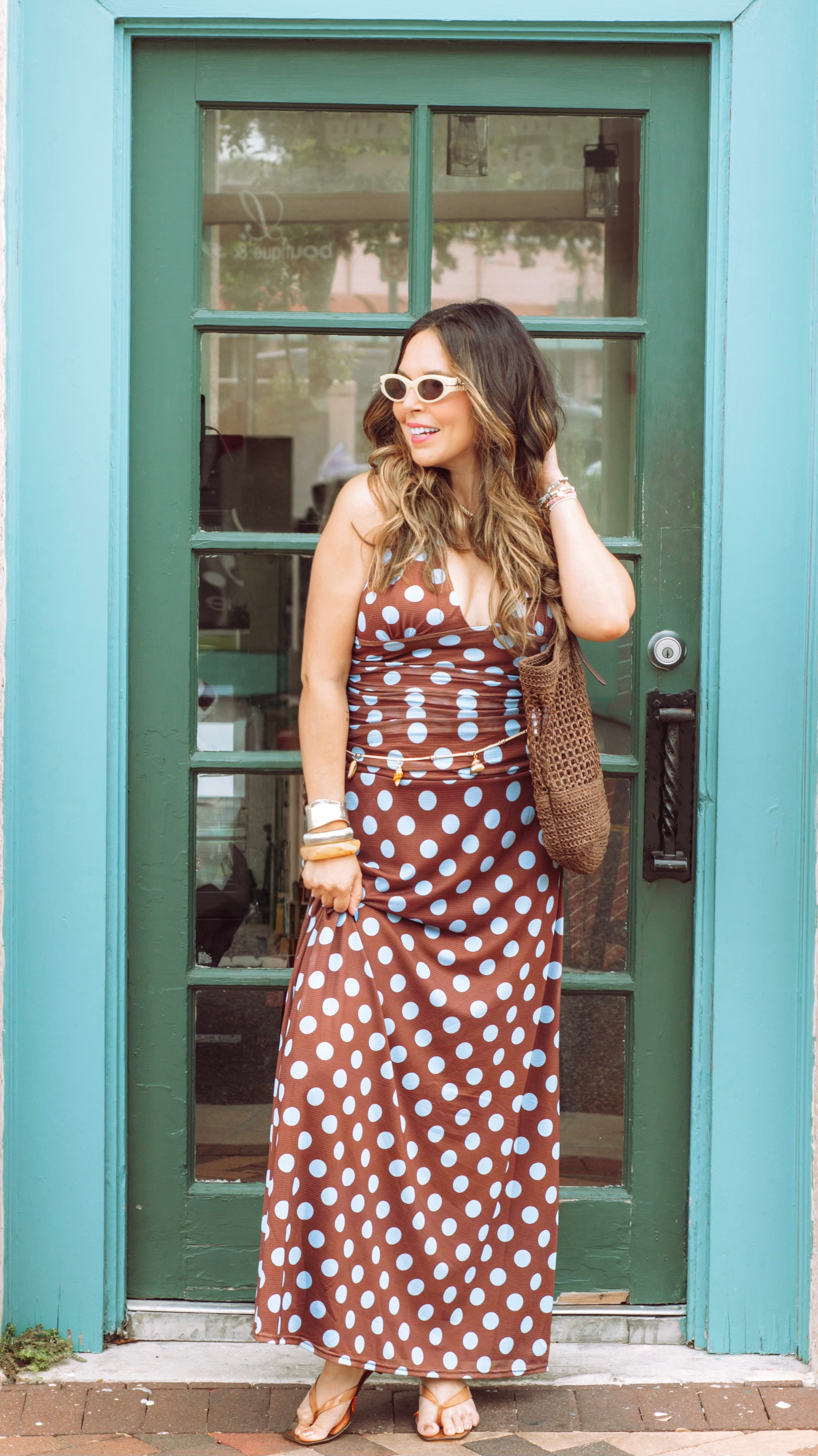 Woman in a polka dot dress standing in front of a teal door.