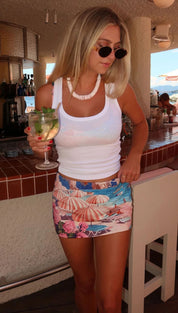 A vibrant, patterned mini skirt featuring a tropical beach scene with striped umbrellas and pink flowers on a blue background.
