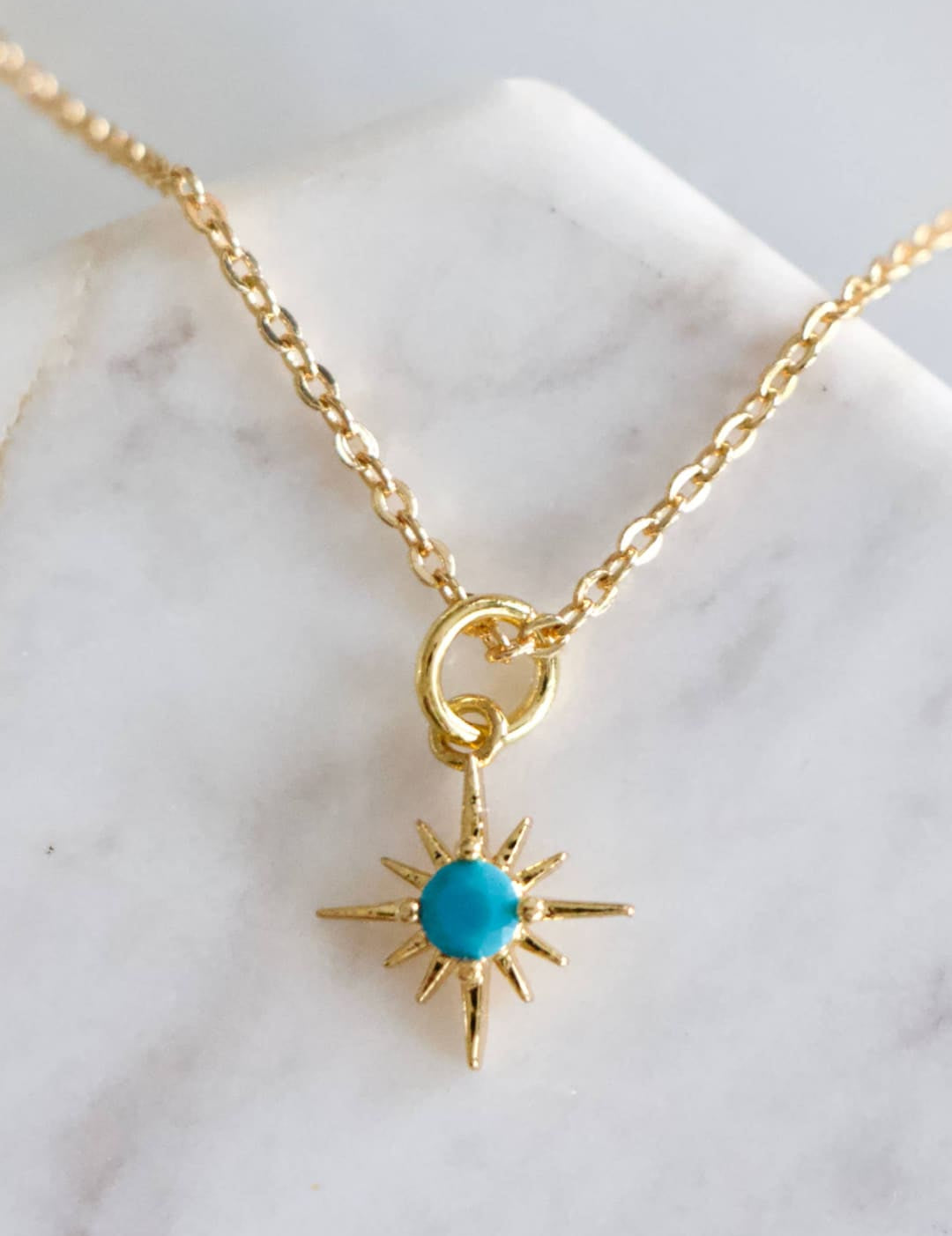 Gold chain necklace with turquoise starburst pendant.