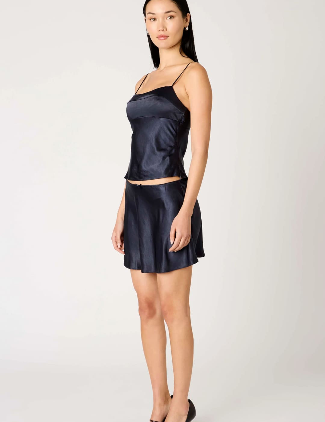 A woman wearing a navy blue satin camisole and matching mini skirt with black heels.