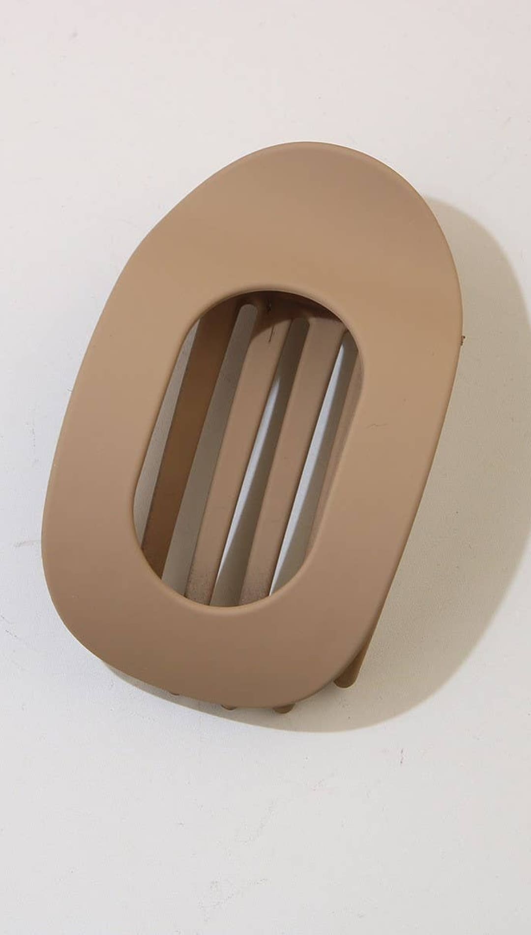 Beige oval-shaped belt buckle with horizontal slits for fastening.